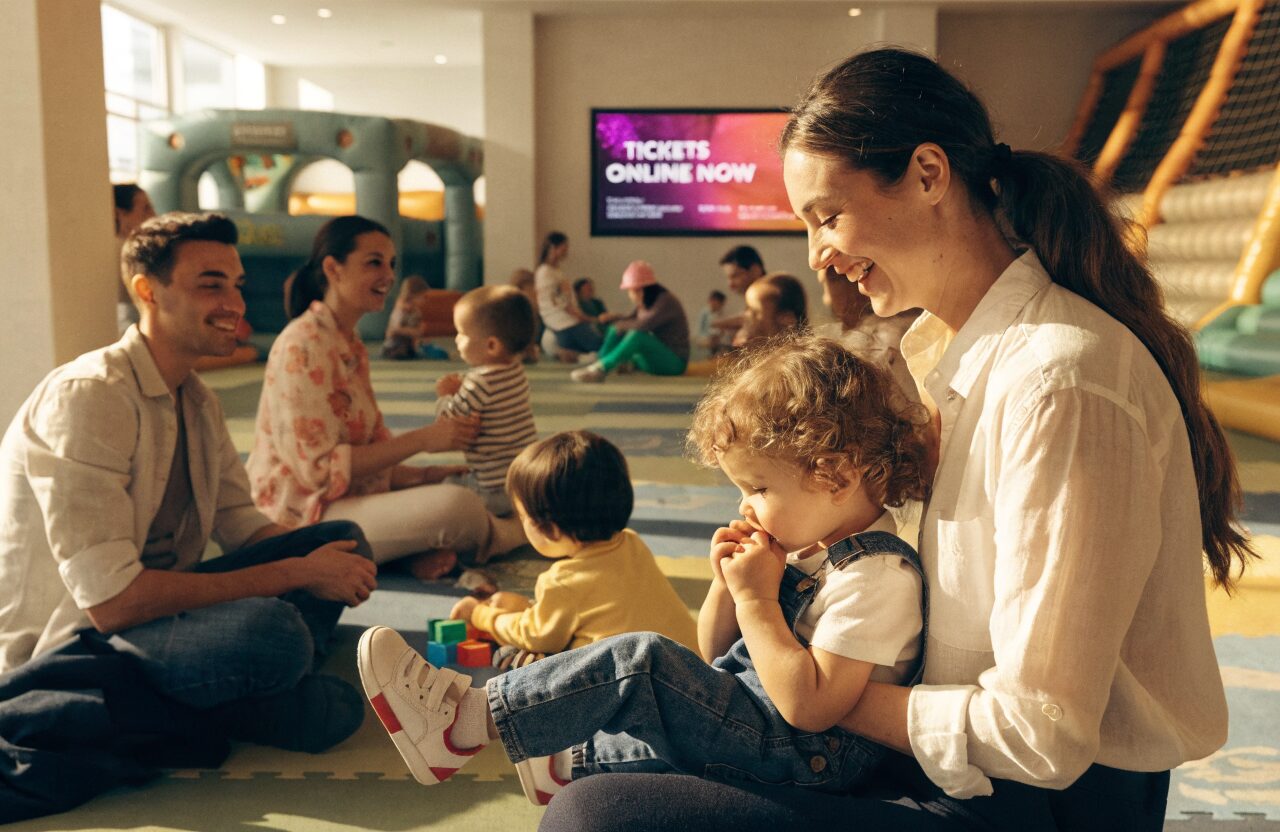 Families with young children enjoying a soft play centre with an advert screen on the wall