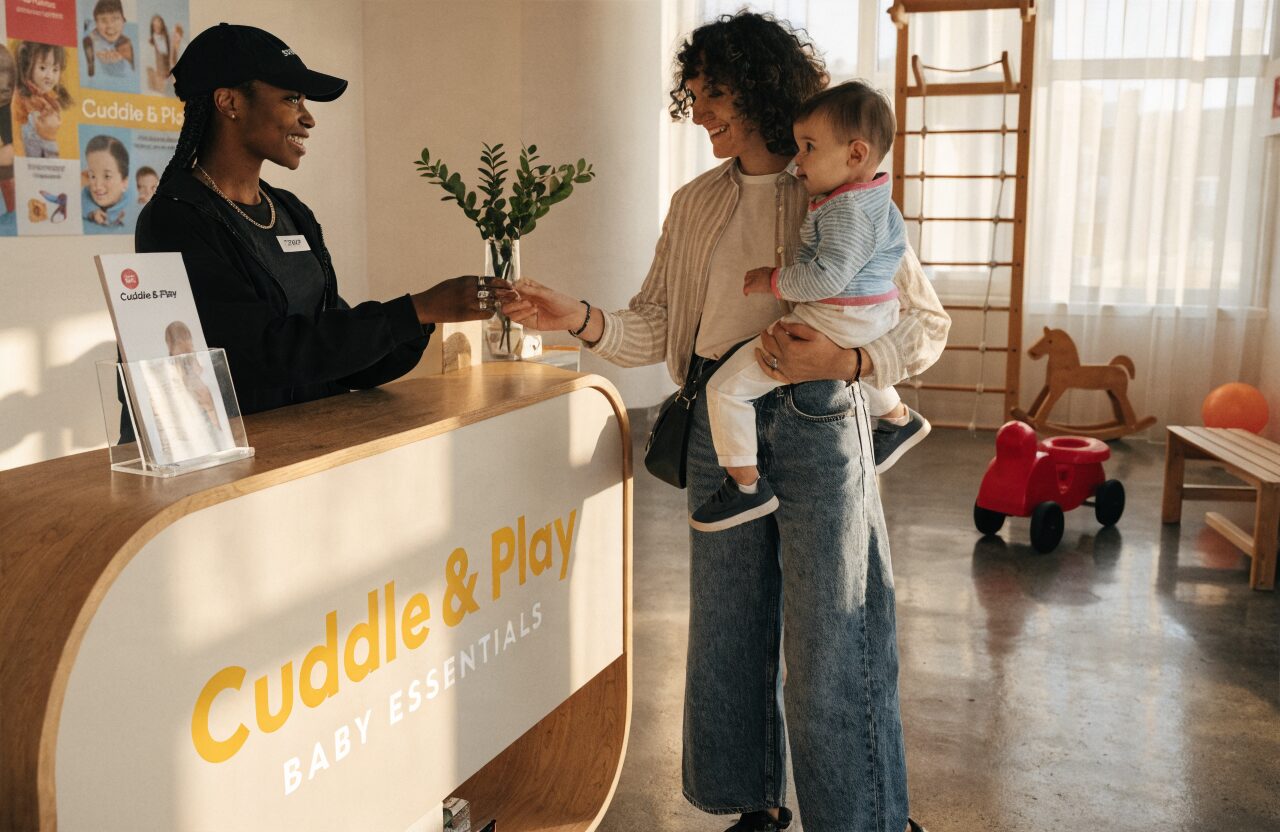A friendly staff member handing a product sample to a parent in a play centre